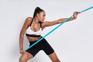 Active young African woman exercising with elastic resistance band against white background photo