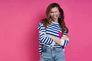 Playful young woman sticking out tongue while standing against colored background photo