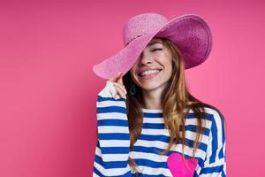 Beautiful young woman adjusting her hat and smiling while standing against colored background photo