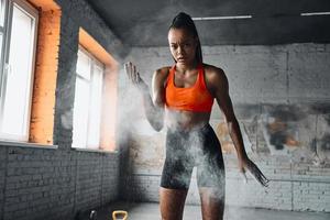mujer joven concentrada usando polvo de talco en las manos antes de entrenar en el gimnasio foto