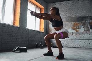 Longitud total de una joven africana que usa una banda de resistencia elástica mientras hace ejercicio en el gimnasio foto