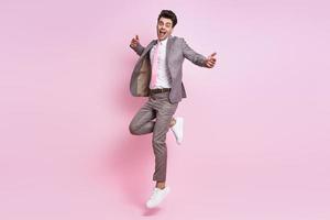 Happy young man in full suit jumping against pink background photo