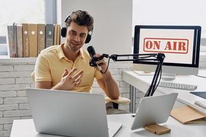 apuesto joven usando micrófono y gesticulando mientras graba podcast en el estudio foto