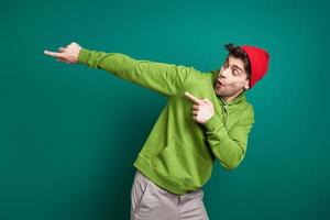 Playful young man pointing away while standing against green background photo