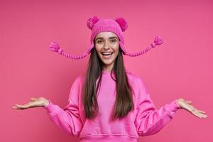 Excited young woman in hooded shirt playing with her funky hat against pink background photo