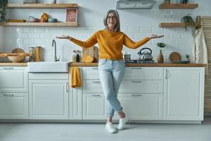 Elegant senior woman gesturing and smiling while standing at the domestic kitchen photo