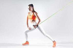 Confident woman in sports clothing using resistance band while exercising against white background photo