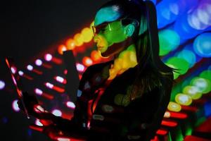 mujer segura de sí misma con gafas futuristas usando una tableta digital contra un fondo colorido foto