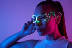 joven segura de sí misma ajustando gafas futuristas contra un fondo oscuro foto