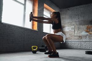 Concentrated young African woman lifting weights while exercising in gym photo