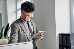 joven concentrado que usa una tableta digital mientras trabaja en la oficina foto