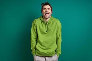 Happy young man laughing and keeping eyes closed while standing against green background photo