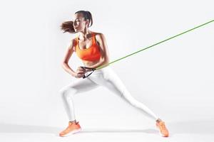 Beautiful young woman using resistance band while exercising against white background photo