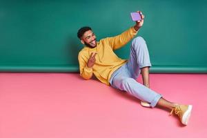 Playful African man making selfie and grimacing while lying against colorful background photo
