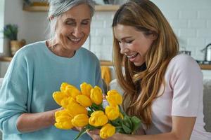 Happy senior mother receiving a bunch of tulips from her daughter while sitting at home together photo