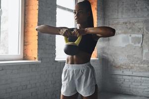 Concentrated young African woman exercising with kettlebell in gym photo