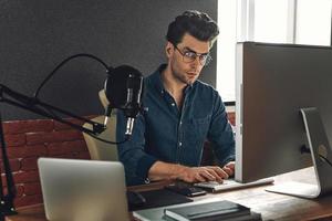 Confident young man using computer while sitting at radio station office photo