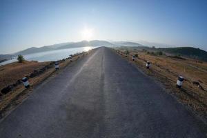 Sunrise at the reservoir, clear blue sky, wide angle from Lens Fisheye, straight road ahead over the dam,March 9, 2019, Khlong Din Daeng Reservoir, Nakhon Si Thammarat, Thailand photo