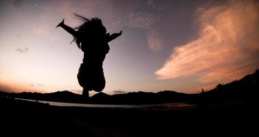 silueta, feliz saltando sombra chica salta sobre el cielo naranja por la noche foto