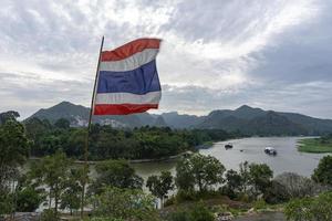 bandera tailandesa soplada por el viento, el fondo es la vista del río kwai y las montañas de kanchanaburi, tailandia foto