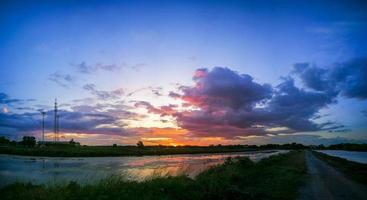 panorama el estanque refleja la luz del sol naranja. el borde de la piscina es hierba verde y amarilla. el cielo de la tarde antes de la puesta del sol es colorido. foto