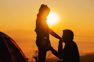 silhouette couple love concept - man hold and kiss woman hand in warm morning sun silhouette during his camping with sea of mist or fog in high mountain area of chiang mai north of thailand photo