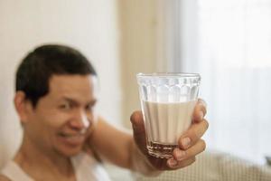Asian man drink milk after wake up in the morning sitting on a bed - health care concept photo