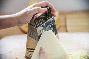 mujer preparando queso para cocinar usando rallador de queso en la cocina - gente haciendo comida con concepto de queso foto