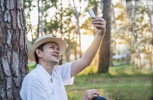 Asian man with mobile phone in forest tree nature - people in spring nature and technology concept photo