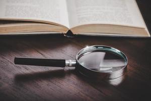 open book with magnifying glass on wooden desk in information library of school or university, concept for education,reading , study, copy space on table background. photo