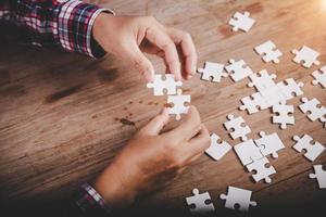 Hands holding jigsaw puzzles piece on wooden table background, success business, solution strategy, teamwork partnership concept photo