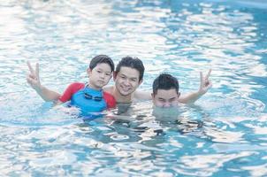 Father and his two son play in clear water swimming pool - happy family play time concept photo