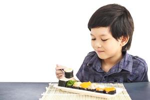 Chico encantador asiático está comiendo sushi aislado sobre fondo blanco. foto