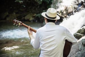 Man play ukulele new to the waterfall - people and music instrument life style in nature concept photo