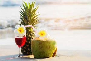 Cocktail glasses with coconut and pineapple on clean sand beach - fruit and drink on sea beach backgroudn concept photo