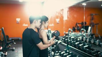 jeune femme en forme faisant de l'exercice avec des haltères dans la salle de sport avec un entraîneur masculin video