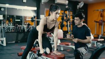 mujer joven en forma haciendo ejercicio con pesas en el gimnasio con entrenador masculino