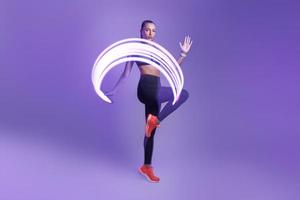 mujer joven confiada en ropa deportiva haciendo ejercicio contra el fondo violeta foto