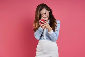 Shy young woman holding smart phone and covering face with hand against colored background photo