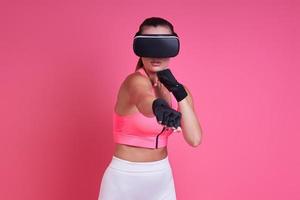 Young woman in virtual reality glasses boxing against pink background photo