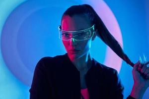 mujer joven confiada en gafas futuristas de pie contra un fondo colorido foto