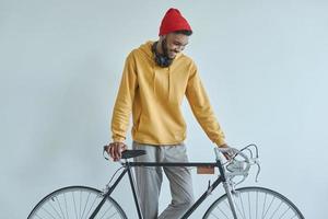 Happy young African man examining his bicycle while standing against the wall photo
