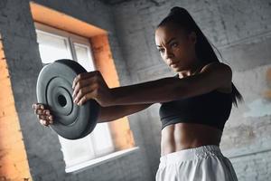 mujer africana joven concentrada levantando pesas mientras hace ejercicio en el gimnasio