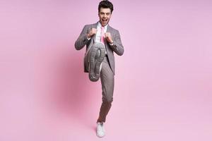 Angry young man in full suit throwing leg kick while standing against pink background photo