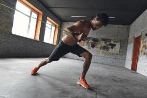 Concentrated young man exercising with elastic resistance band in gym photo