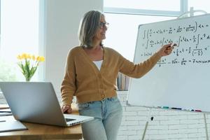 Confident senior woman pointing whiteboard and smiling while standing at the classroom photo