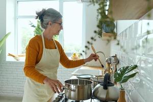 Confident senior woman cooking at the domestic kitchen photo