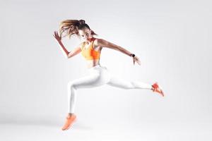Hermosa mujer joven en ropa deportiva corriendo contra el fondo blanco. foto
