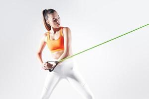 Concentrated woman using resistance band while exercising against white background photo