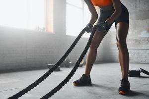 Close-up of unrecognizable woman preparing for training with battle ropes in gym photo